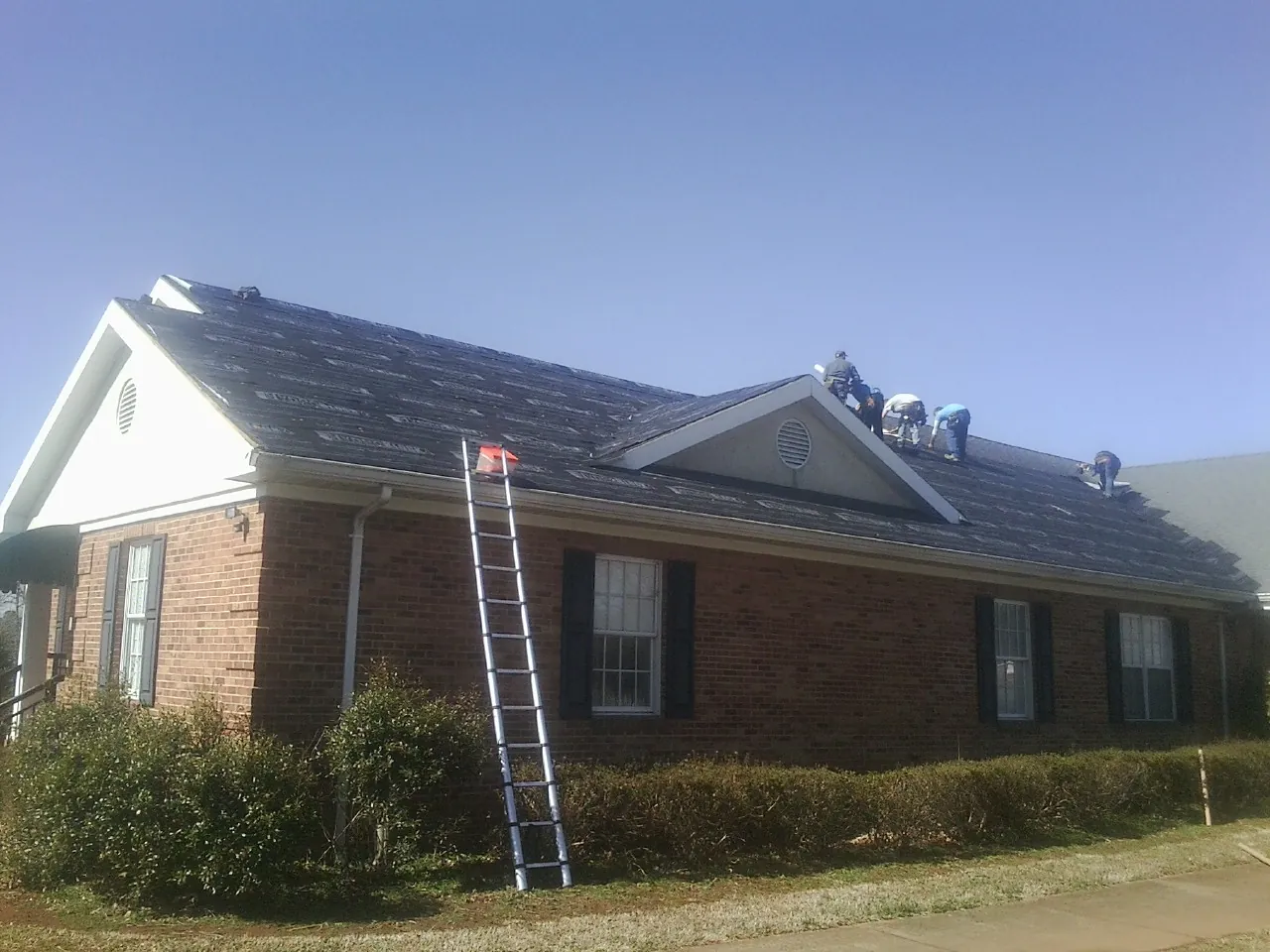 Crew tearing shingles off a brick ranch roof with a ladder set — Emergency Roof Repair work by our crew in Roselle