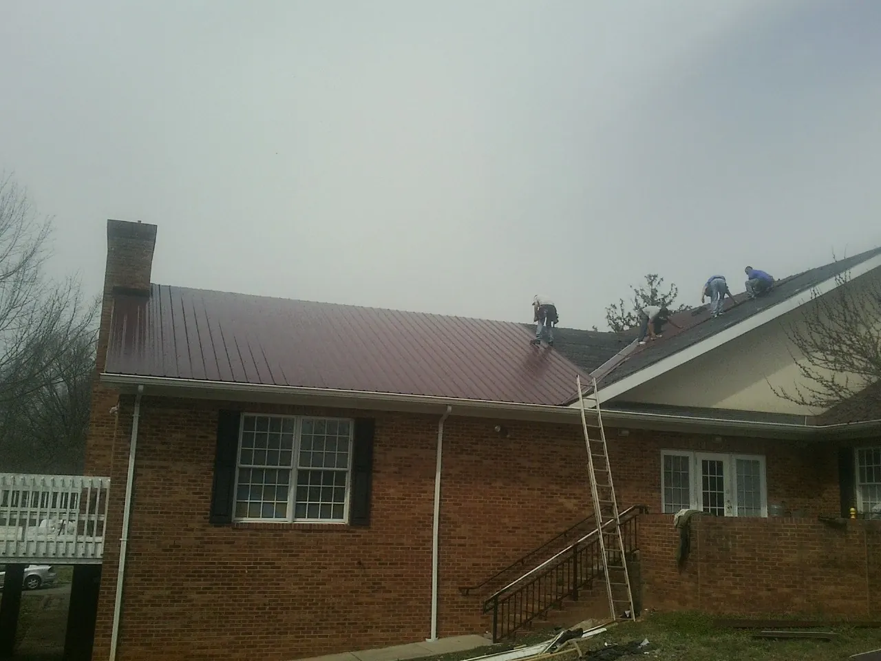 Crew setting red metal roofing panels on a brick home in Roselle