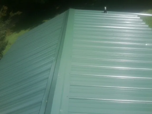 New green metal panels meeting at the ridge of a roof — Flat Roof Repair work by our crew in Roselle